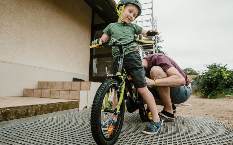 Father assisting young son with bicycle in backyard, teaching safe riding.